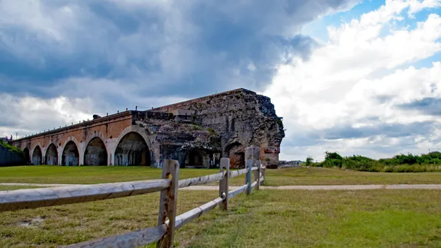The corner of a fort stands on a grassy field with wooden fencing and clouds in the background. — Gulf Islands National Seashore, NPS